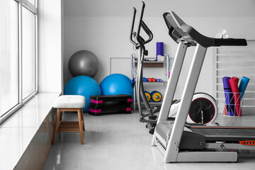 Interior of gym with modern treadmill and sport equipment near window