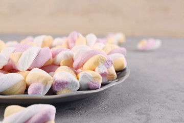 Plate with delicious twisted marshmallows on grey table