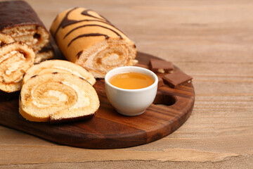 Board with pieces of delicious sponge cake roll, bowl of jam and chocolate on wooden table