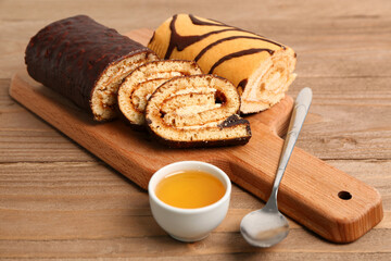 Board with pieces of delicious sponge cake roll and bowl of jam on wooden table