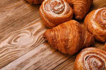 Delicious croissants and cinnamon rolls on wooden background