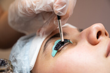 Close-up portrait of a woman on eyelash lamination procedure. The master applies tint to the eyelashes. 