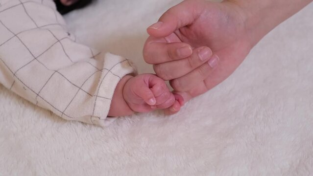 乳児の赤ちゃんの小指と大人の小指を交わして指切りしている動画