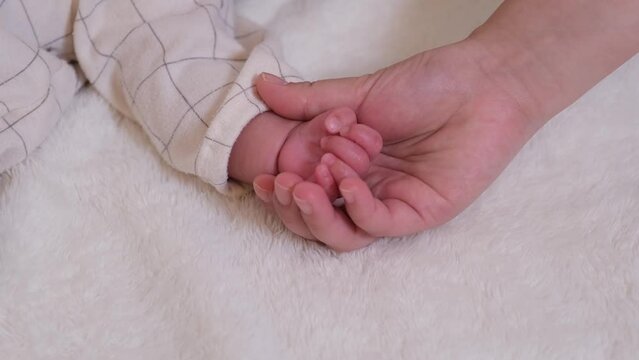 乳児の赤ちゃんの手を大人の手が下からすくって握る動画