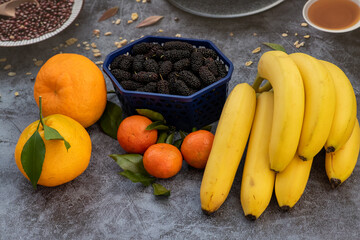 Bunch ripe yellow bananas, black mulberries and tangerines on gray concrete background