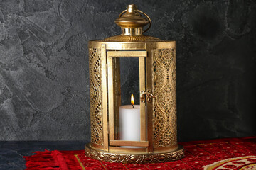 Lantern with burning candle and carpet on dark background. Islamic New Year celebration