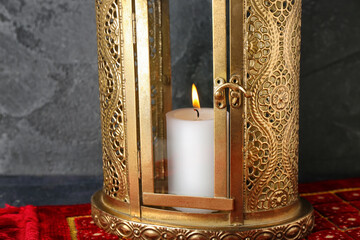 Lantern with burning candle and carpet on dark background, closeup. Islamic New Year celebration
