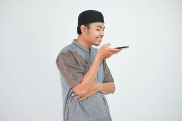 young Asian Muslim man smile talking using the voice assistant on mobile phone wearing muslim clothes isolated on white background