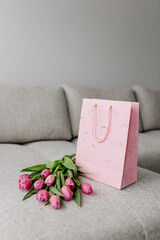 A bouquet of pink fresh tulips lies on a beige fabric and a pink gift bag. Valentine's Day background