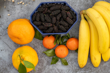 Assortment of tropical fruits, banana, orange, tangerine, mulberry on dark background, copy-space.