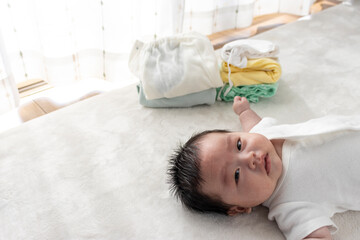 起きている赤ちゃんと畳んだ子供服（0歳2か月、日本人、男の子） - obrazy, fototapety, plakaty