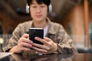 Handsome young Asian man using his smartphone while listening to music through his headphones