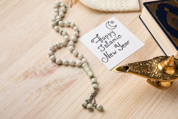 Card with text HAPPY ISLAMIC NEW YEAR, lamp and prayer beads on light wooden background, closeup