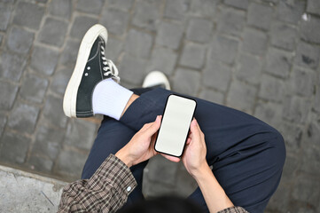 Top view of a man using his smartphone, sitting at the city street. phone white screen mockup