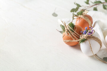 Easter eggs with tied moss and flowers on white table
