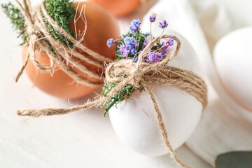 Easter eggs with tied moss and flowers on white background, closeup