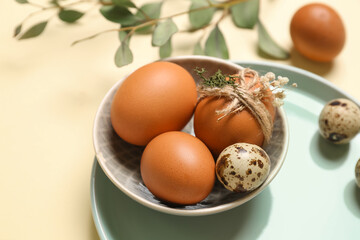 Bowl with Easter eggs on yellow background