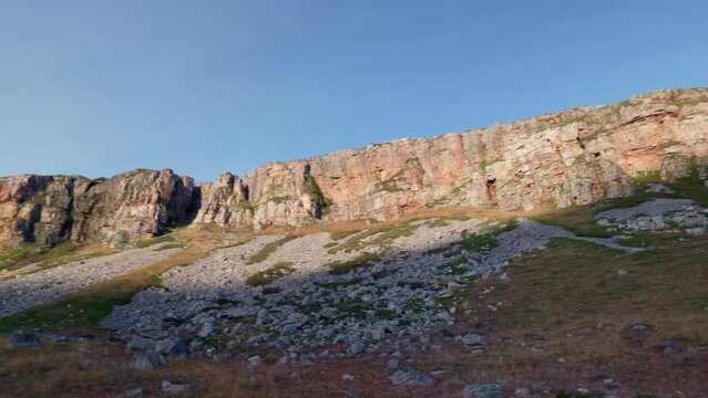 A slow panning shot of an imposing cliff face in the north west highlands as the evening sun sets and rays of light catch the ridge. Loch Gleann Dubh, Scotland.
