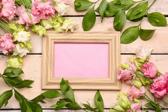 Composition with blank picture frame and flowers on light wooden background
