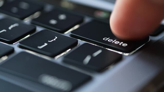Finger of the computer user, he presses the delete button on the computer keyboard.