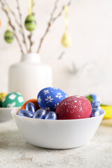 Bowl with painted Easter eggs and candies on light table
