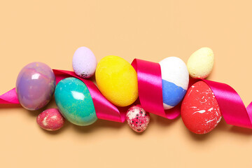 Composition with painted Easter eggs and ribbon on color background, closeup