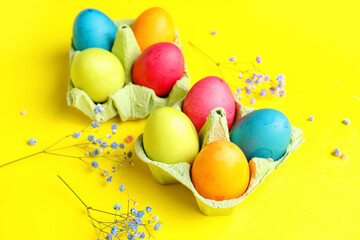 Fototapeta na wymiar Cardboard holders with painted Easter eggs and gypsophila flowers on yellow background