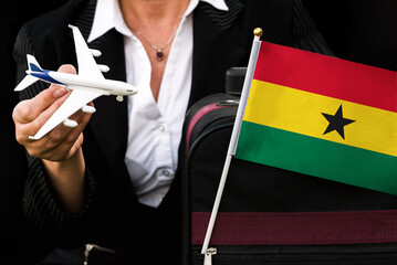 business woman holds toy plane travel bag and flag of Ghana
