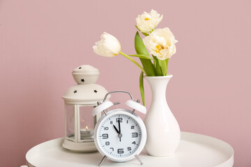 Vase with tulip flowers, alarm clock and lantern on table near color wall