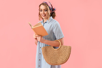 Pretty young woman with wicker bag reading book on pink background