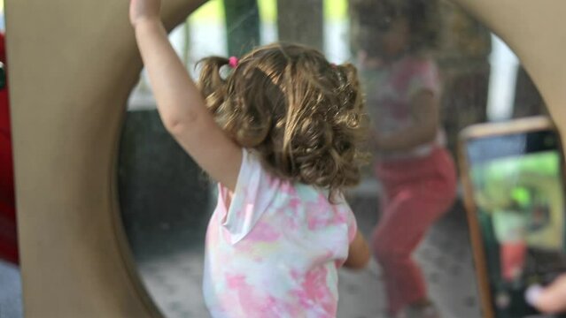 Mother taking picture of her little girl in front of big mirror at playground