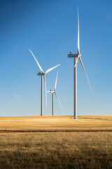 Portrait orientation of windmills standing tall on harvested agriculture fields on the Canadian...