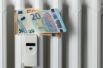 Euro banknotes on a heating radiator battery with a heat meter. Expensive heating costs and rising...