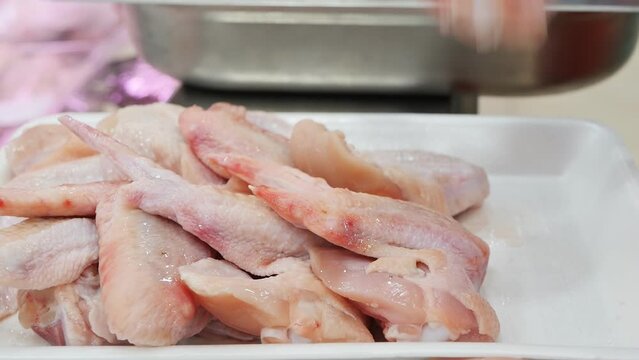 The hands of a poultry farm worker in gloves put raw chicken wings in a foam tray for packing and retailing in a butcher shop. Food industry, poultry farming. chicken meat