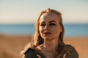 Portrait blonde sea cape. A calm young blonde in an unbuttoned khaki raincoat stands on the seashore, under the raincoat there is a black skirt and top