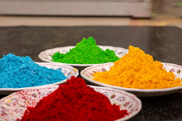 Organic red, green, blue and yellow herbal gulal or Holi colors on a black wooden background. Selective focus.