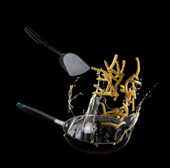 Fried potatoes(French fries) up from a Iron frying pan with oil splash Isolated on black background