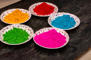 Organic red, green, blue and yellow herbal gulal or Holi colors on a black wooden background. Selective focus.