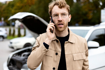 Unhappy man driver calling car service, having engine problem standing near broken car with open...