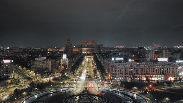 Aerial hyperlapse shot of traffic on road with roundabout and Parliament Building of Bucharest in background at night