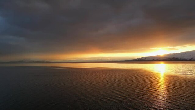 Panning aerial view over Utah Lake reflecting the sunset in the water during winter.