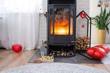 Valentine decor near fireplace stove with fire and firewood. Cozy home hearth in interior with...