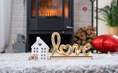 Key to house with keychain against background of fireplace stove with fire and firewood in Valentine decor, love home. Moving to new house, mortgage, rent and purchase real estate