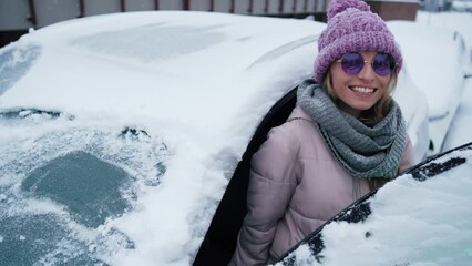 Happy young woman opening car doors and ging out. First snow covered car
