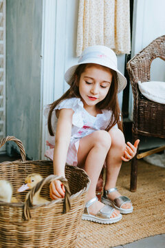 pretty little Armenian girl sit on veranda on sunny spring day decorated with flowers and Easter decor and playing with baby ducks ducklings, Easter family celebration