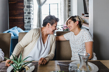 hispanic aged mother and adult daughter hugging and laughing at home in Mexico Latin America