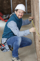 happy builder measures a wall with a tape measure