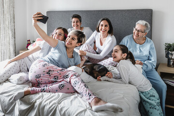 Hispanic happy family of women, grandmother, daughter and children laughing taking a photo selfie on bed at home in Latin America	