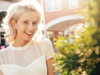 Young beautiful smiling hipster woman in trendy summer dress clothes. Sexy carefree model posing in the street at sunny day. Positive blond female outdoors. Cheerful and happy