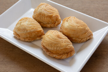 close up of deep fried curry puff in a plate on wooden table. snack and appetizer concept.